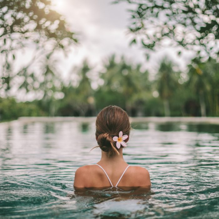 Femme se détendant dans une piscine naturelle, fleur blanche accrochée à son chignon.